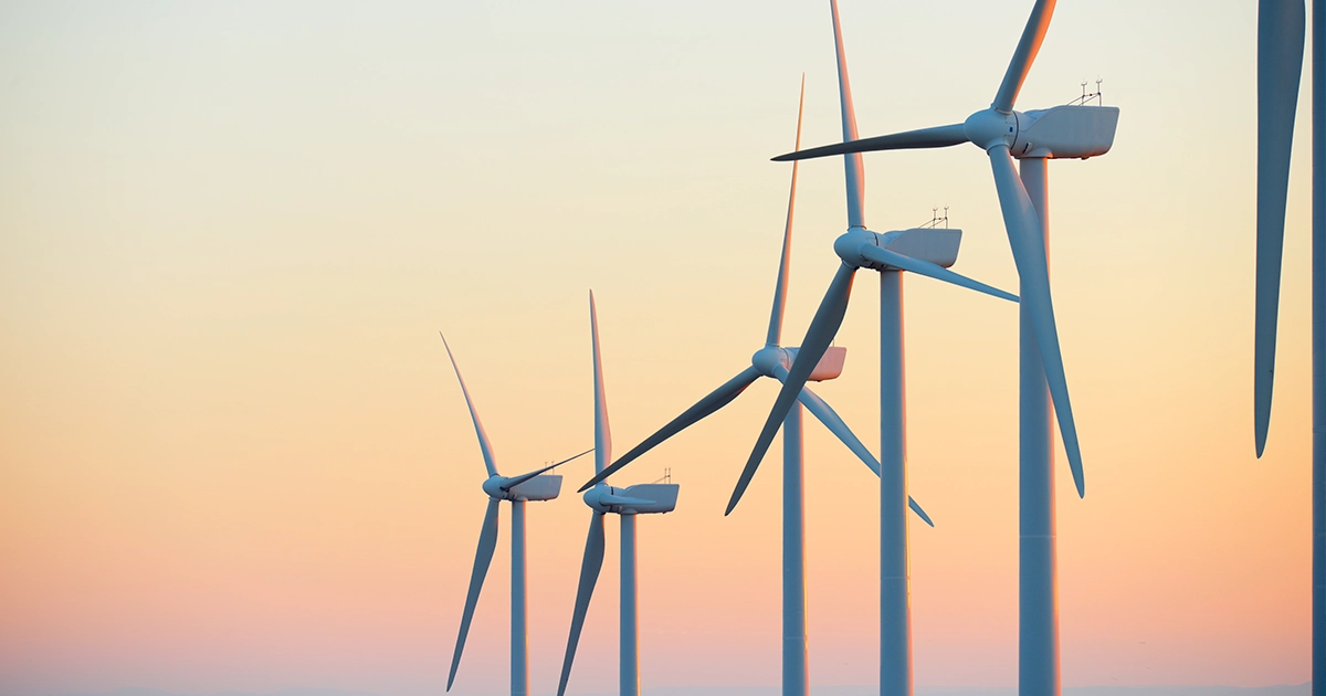 Row of wind turbines at sunrise, representing renewable energy participation in FCAS and the role of power quality monitoring.