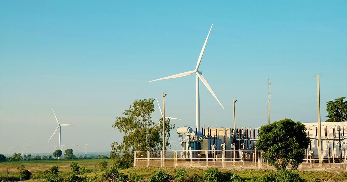 Multiple wind turbines and a substation under clear skies, illustrating grid integration and system data capture for regulatory compliance.