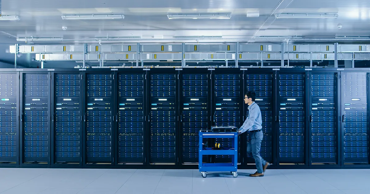 Technician pushes a cart loaded with equipment past a wall of racks in a data centre
